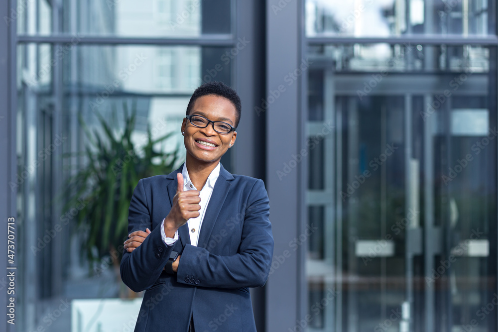 Portrait of young successful business woman, african american woman smiling happy looking at camera, wearing glasses, near modern office Portrait of young successful business woman, african american woman smiling happy looking at camera, wearing glasses, near modern office