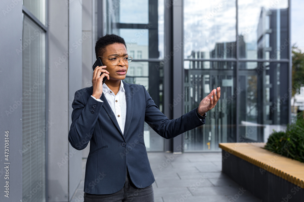 Serious and nervous business woman with glasses, African American woman with short haircut talking on the phone, outside the office Serious and nervous business woman with glasses, African American woman with short haircut talking on the phone, outside the office