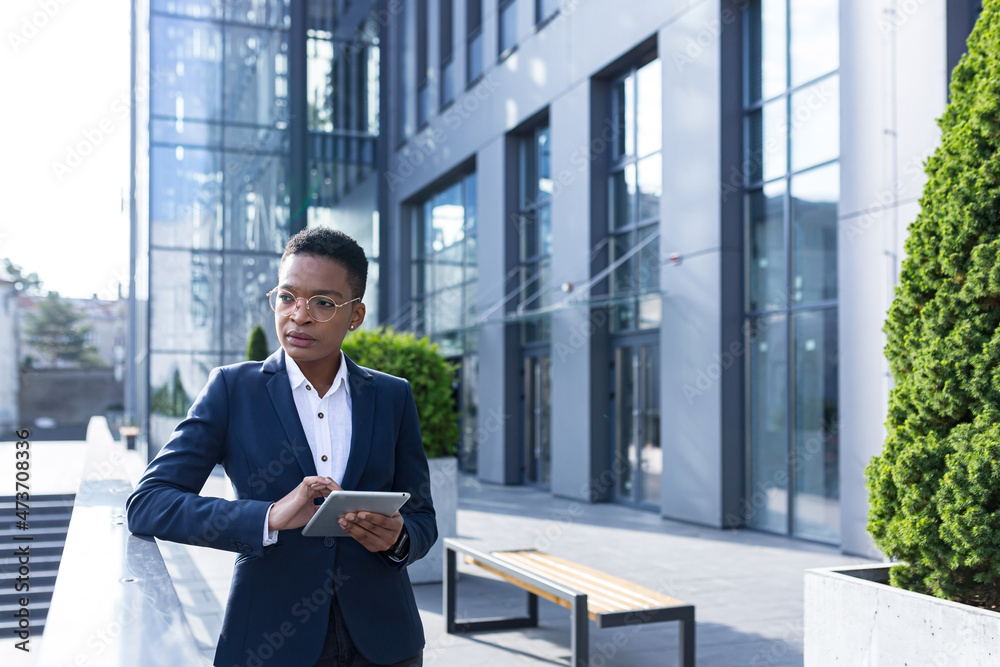 Fototapeta premium Serious and thinking business woman African American on a break near the office, uses a tablet online, reads statistics uses the application