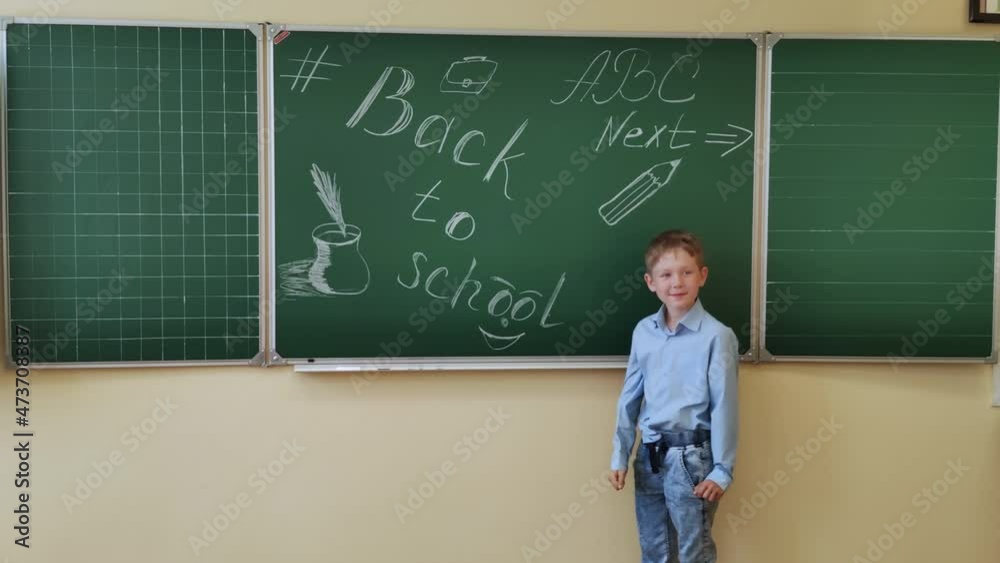 An 8-9 year old student at the blackboard shows the class with his thumb. An 8-9 year old student at the blackboard shows the class with his thumb.