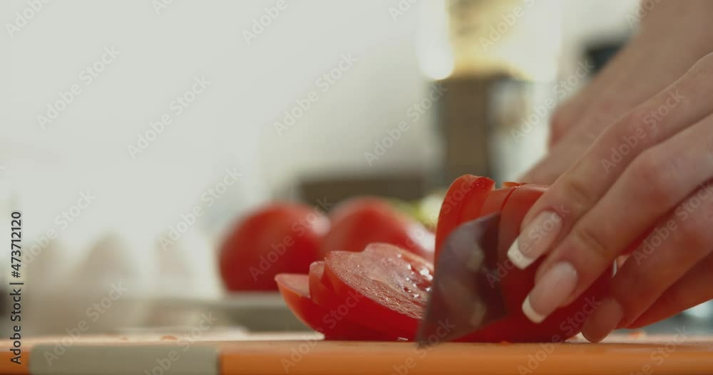 Woman's hands using kitchen knife cutting fresh tomato on wooden cutting board. Healthy eating.