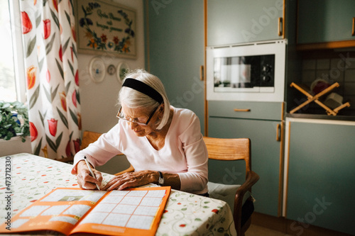 Senior woman solving sudoku at dining table in kitchen photo