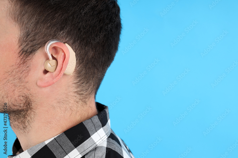 Fototapeta premium Young man with hearing aid on blue background