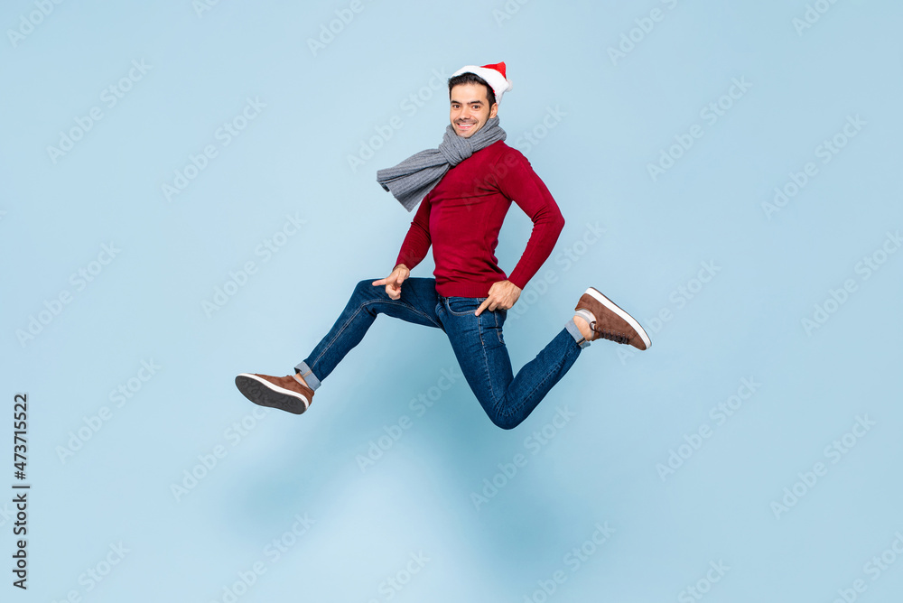 Young happy handsome Caucasian man in Christmas outfit jumping in isolated color light blue background