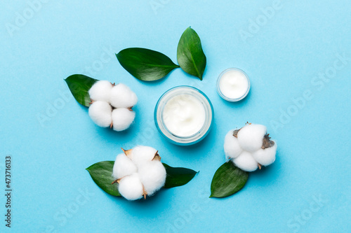 Organic cosmetic products with cotton flower and green leaves on color background. Flat lay
