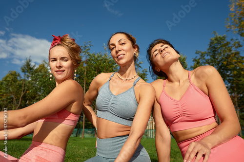 Smiling fitness women in training wear talking to each other standing on a street. Three women joggers standing on a street during their morning jog