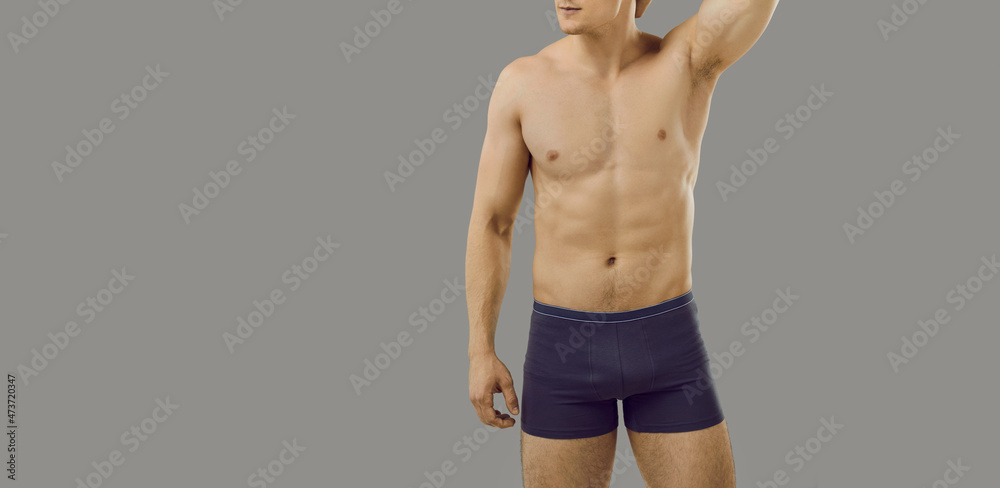 Fototapeta premium Attractive, flirty and coquettish muscular man with perfect athletic body posing in underwear on background. Cropped image of man with naked torso straightening his hair near copy space. Banner.