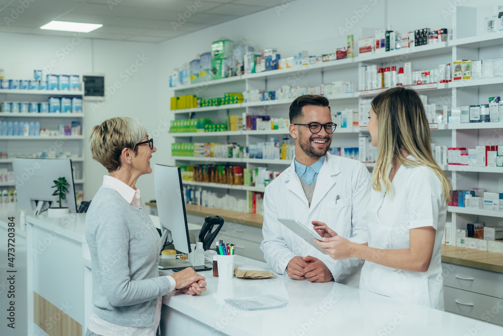 Two pharmacist giving prescription medications to senior female customer in a pharmacy