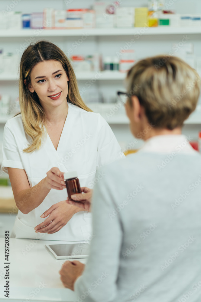 Female pharmacist selling medications at drugstore to a senior woman customer Female pharmacist selling medications at drugstore to a senior woman customer