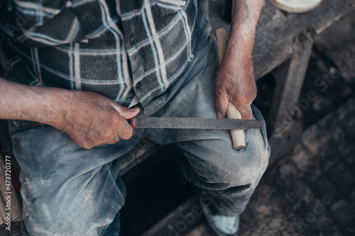 Hands of a senior carpenter working on a piece of wood with a file