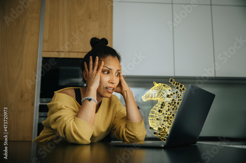 Woman with head in hands looking at Trojan virus icon on laptop