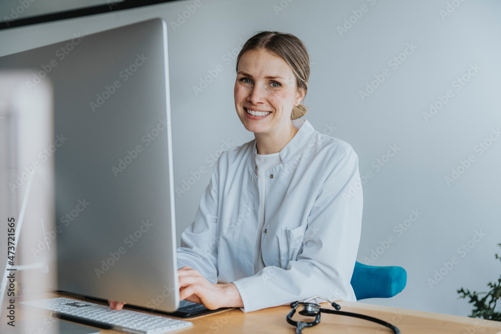 Smiling female expertise sitting by computer at desk Smiling female expertise sitting by computer at desk