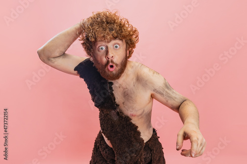 Cropped portrait of man in character of neandertal scratching back of his head isolated over pink background photo