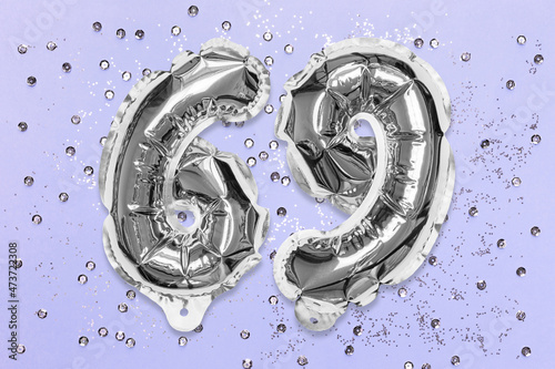 Silver foil balloon number, digit sixty nine on a lilac background with sequins. Birthday greeting card with inscription 69. Top view. Numerical digit. Celebration event, template. photo