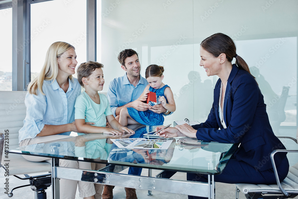 © Westend61 - Smiling female real estate agent discussing with family sitting at table © Westend61 - Smiling female real estate agent discussing with family sitting at table