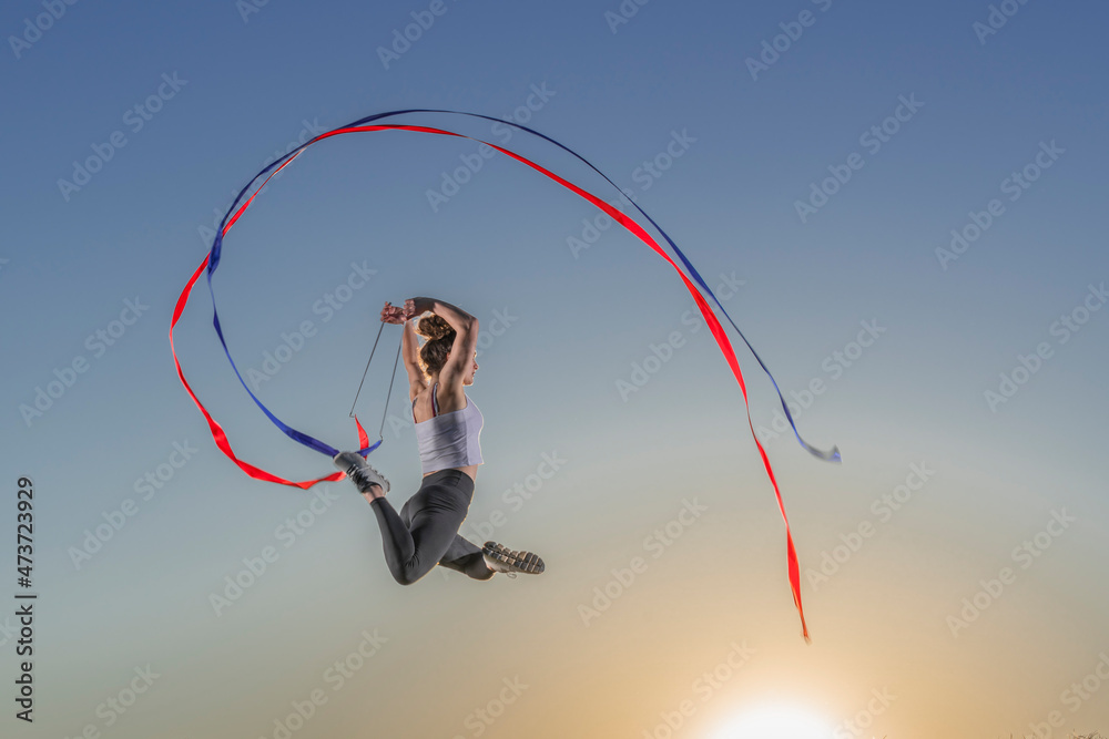 Female gymnast jumping with ribbons during sunset Female gymnast jumping with ribbons during sunset