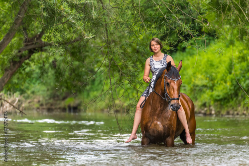 Young woman riding horse in river at forest