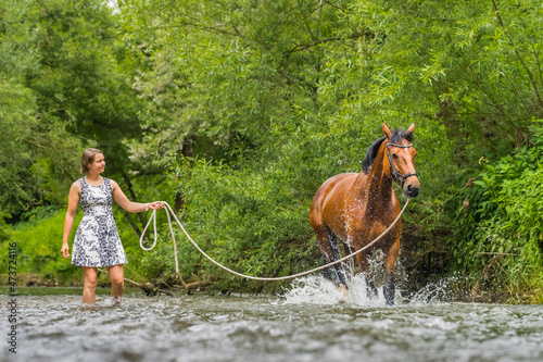 Young woman guiding horse on longe splashing in water photo