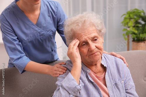 Nurse taking care of senior woman with headache indoors photo