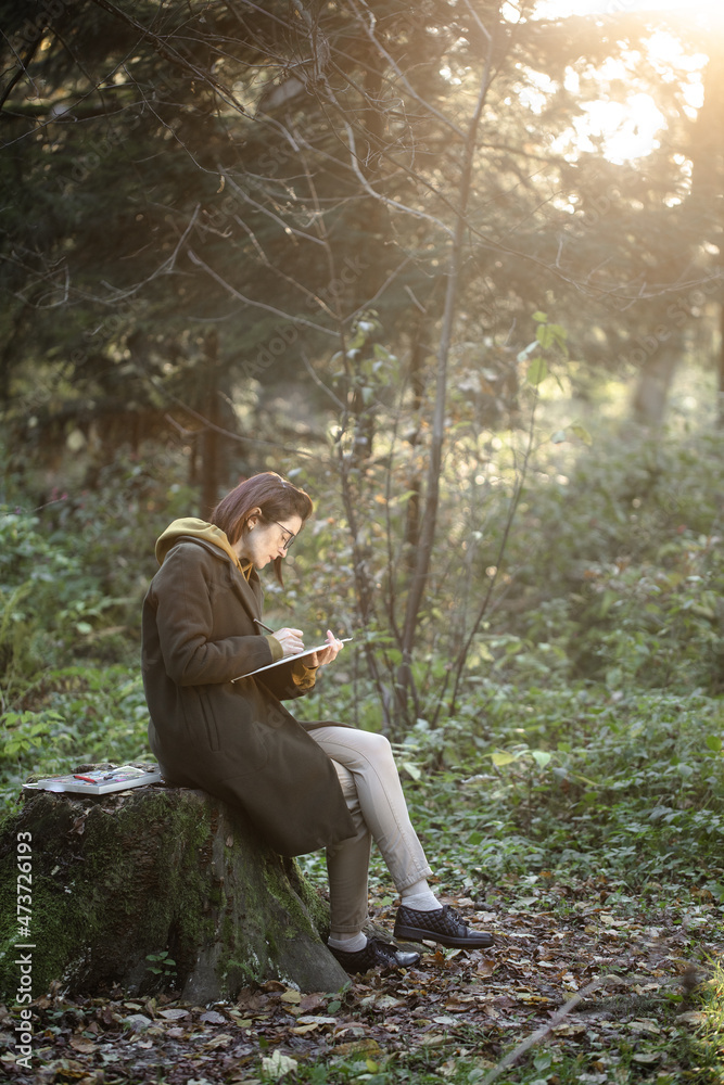 A girl draws in a sunny forest