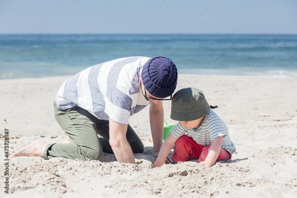 Father and son digging sand together while playing at beach during sunny day Father and son digging sand together while playing at beach during sunny day