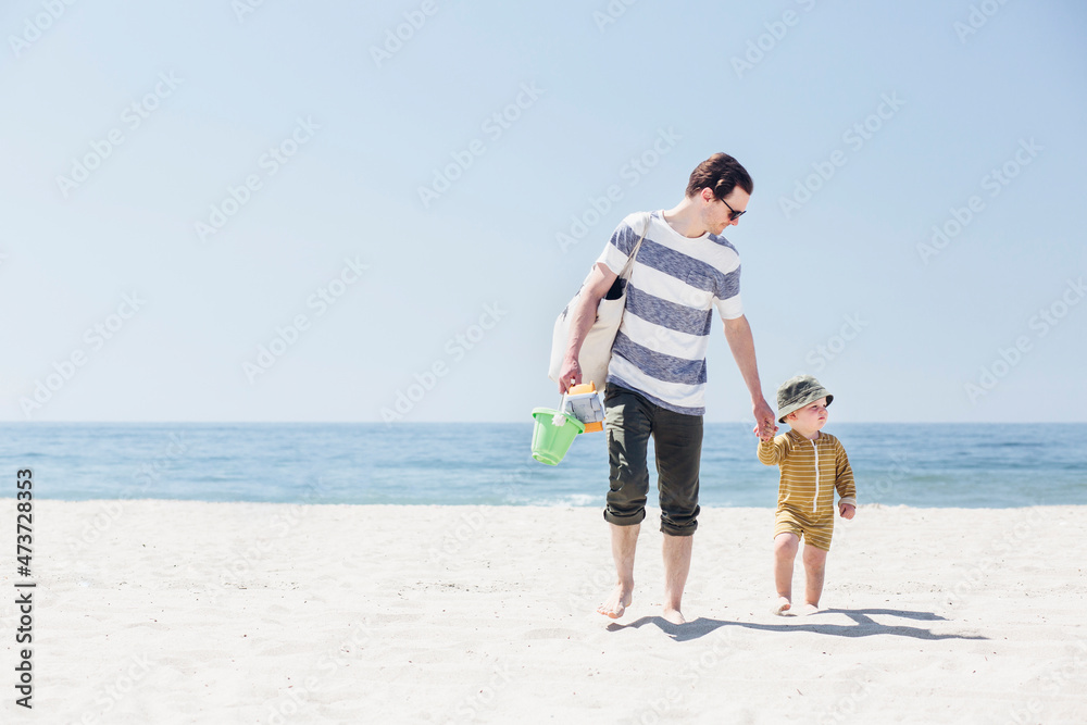 Father and son holding hands while walking at beach Father and son holding hands while walking at beach