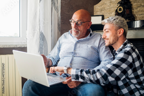 Smiling son guiding father using laptop at home