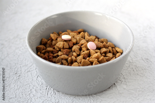 Dry food and vitamins for cats and dogs in a gray bowl. Gray background, close-up. Selective focus.