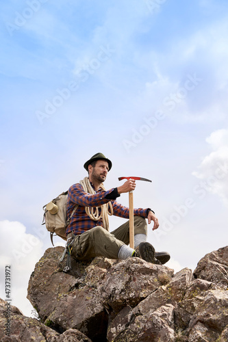 Mountaineer with backpack and axe sitting on rock photo