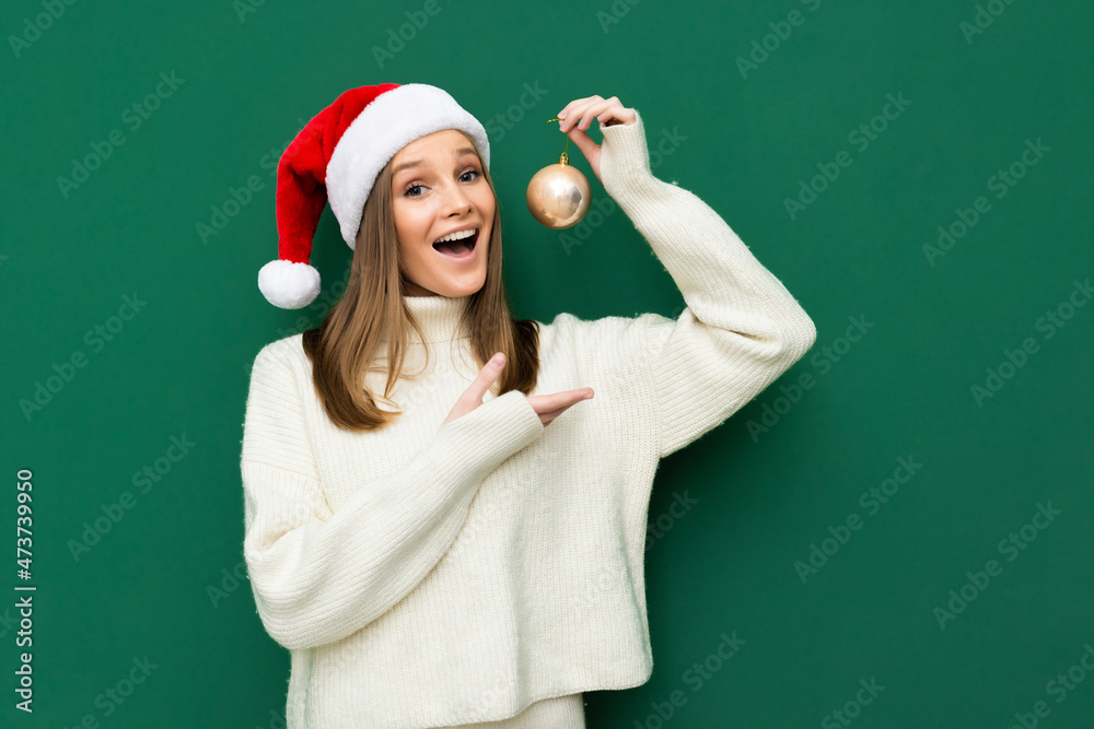 Photo of young woman happy positive smile hold hands balls decor christmas santa hat isolated over green color background Photo of young woman happy positive smile hold hands balls decor christmas santa hat isolated over green color background