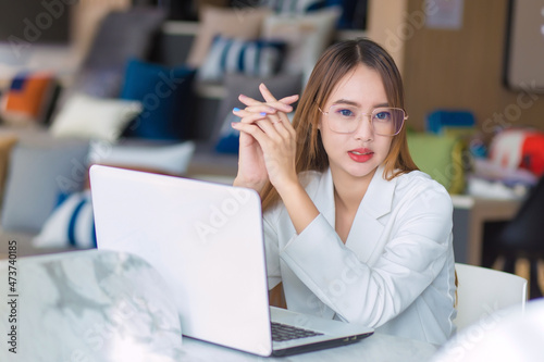 Asian professional business woman wearing glasses works while looking at the camera and sitting work.at co-working space with laptop,paper work (Business woman concept).