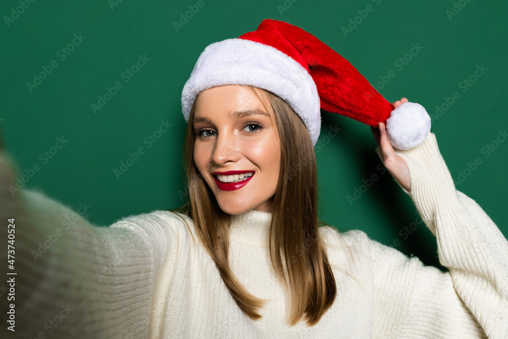 Young woman happy positive smile make selfie wear santa hat winter season isolated over green color background