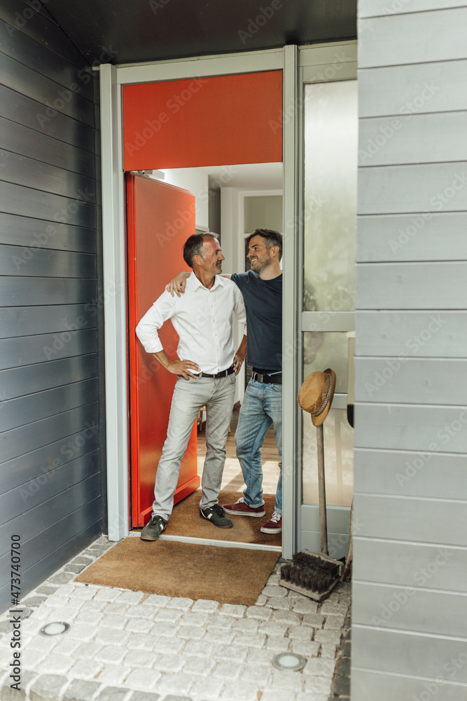 Son with arm around father standing at house entrance Son with arm around father standing at house entrance