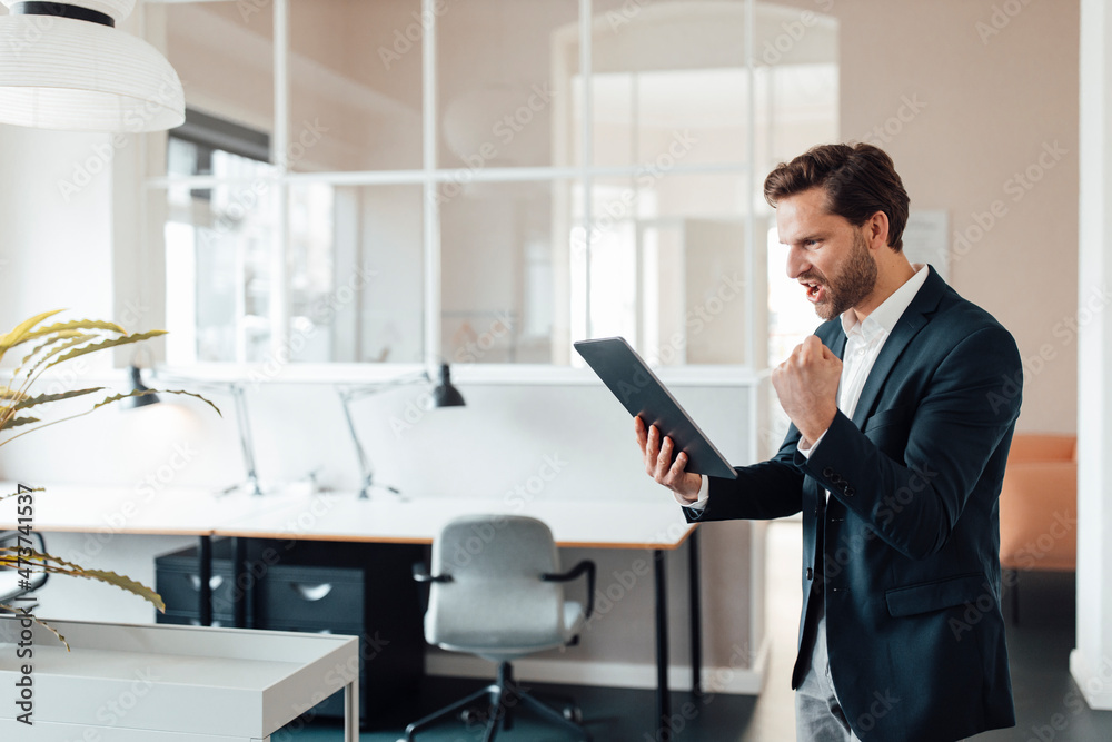 Businessman cheering while using digital tablet in office Businessman cheering while using digital tablet in office