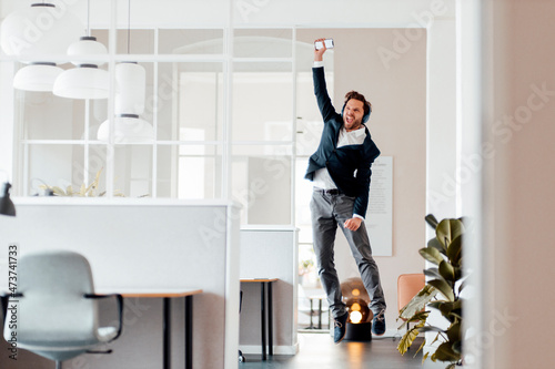 Businessman with mobile phone cheering while jumping in office photo