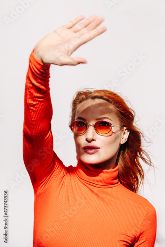 Young woman in orange outfit using hand to avoid light