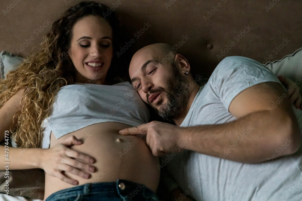 Man touching pregnant woman's abdomen while lying on bed at home Man touching pregnant woman's abdomen while lying on bed at home
