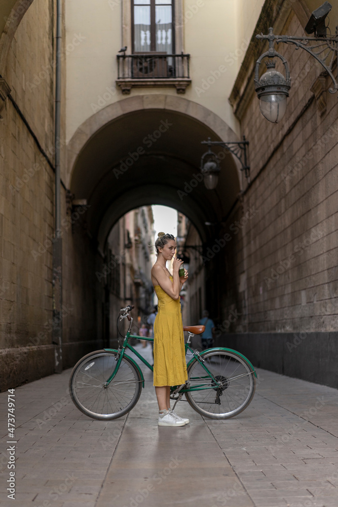 Woman drinking smoothie while standing with bicycle on footpath Woman drinking smoothie while standing with bicycle on footpath