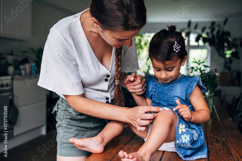Mother holding hand while putting bandage on daughter's knee at home