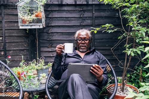 Male professional holding mug looking at digital tablet while sitting on chair in backyard photo
