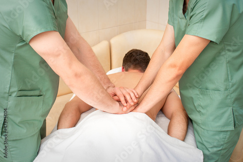 Young man receiving back massage in four hands in spa beauty salon