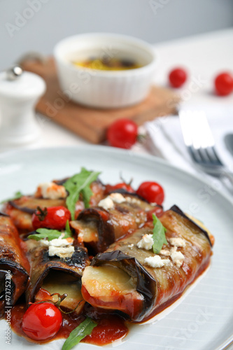 Delicious baked eggplant rolls with tomatoes, cheese and arugula on plate, closeup