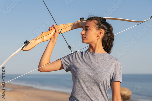 Woman with bow and arrow looking away while standing at beach photo