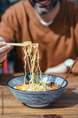 Handsome mature man eating ramen with chopsticks in an asian restaurant photo