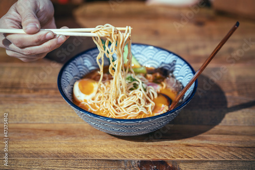 Handsome mature man eating ramen with chopsticks in an asian restaurant photo