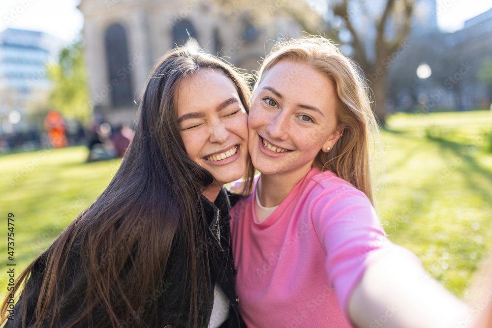 Happy women with cheek to cheek standing in public park Happy women with cheek to cheek standing in public park