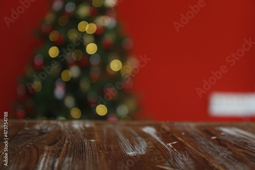 Blurred out traditional christmas pine tree with holiday decorations  wooden plank board with copy space for text. Decorative lights glowing on fir with bokeh effect. Close up  background  interior.