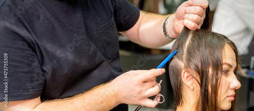 Hairdresser divides female hair into sections with comb holding hair with her hands in hair salon close up