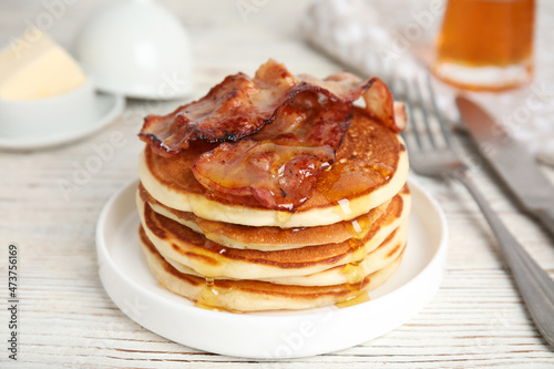 Delicious pancakes with maple syrup and fried bacon on white wooden table, closeup