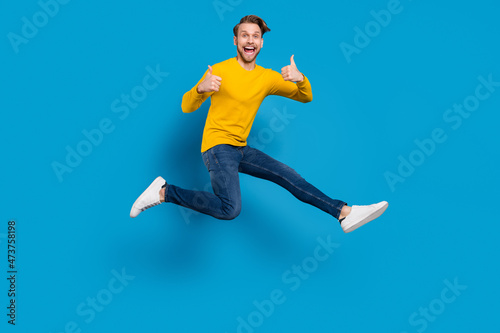 Full length body size of young guy smiling jumping up showing like gesturing isolated vibrant blue color background